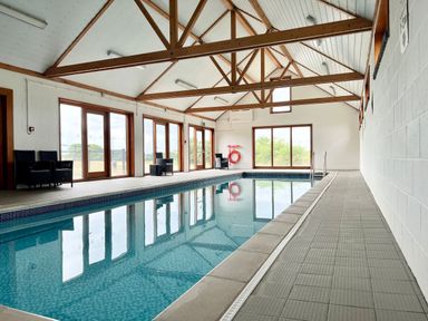 An indoor swimming pool with chairs along the side windows and wooden beams on the ceiling at The Gallery  Blythburgh near Southwold