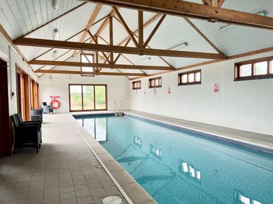 An indoor swimming pool with chairs along one side and wooden beams on the ceiling at The Gallery Blythburgh near Southwold