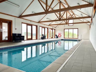 An indoor swimming pool with wooden beams on the ceiling and chairs along the sides at The Gallery Blythburgh near Southwold
