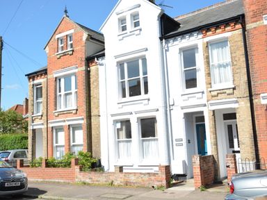 A street view of attached brick and white painted houses with cars parked outside at Driftwood Southwold