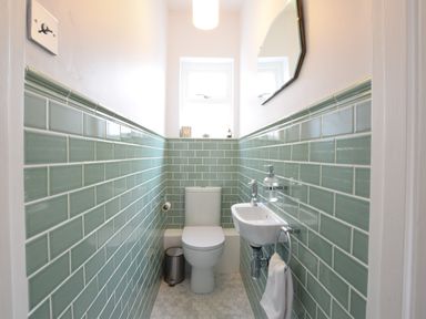 A small bathroom with a toilet sink green wall tiles and a hexagonal mirror at Driftwood Southwold