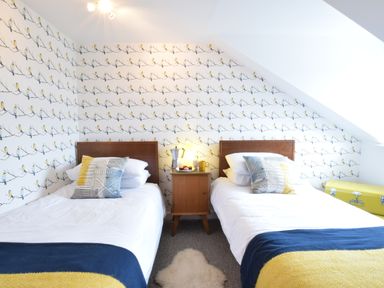 A bedroom with two single beds a wooden bedside table and wallpaper with birds at Driftwood Southwold