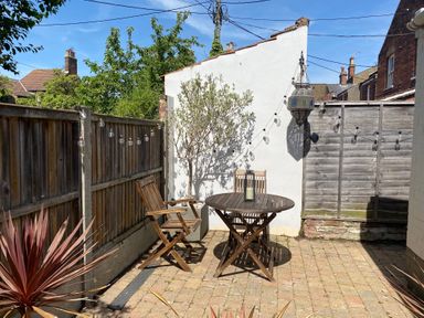 A small patio with a round wooden table and two wooden chairs and string lights on wooden fences at Driftwood Southwold