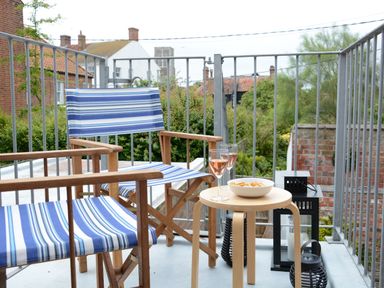 A balcony with two blue striped wooden chairs a small wooden table with two glasses of wine and a bowl of snacks at Driftwood Southwold