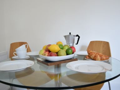 A glass dining table with plates cups a fruit bowl and croissants at Driftwood Southwold