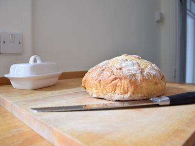 A loaf of bread and a serrated knife on a wooden cutting board in a kitchen at Driftwood Southwold