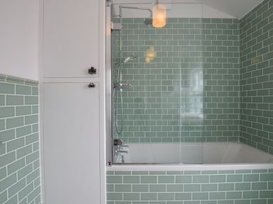 A bathroom with a bathtub shower and green tiled walls at Driftwood Southwold