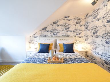 A bedroom with a bed with blue and yellow pillows and a tray with breakfast items Driftwood Southwold