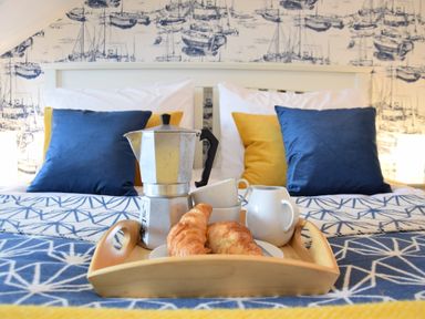 A tray with a coffee pot croissants cups and a jug on a bed with blue and yellow cushions at Driftwood Southwold