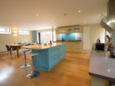 A kitchen with a blue island and beige cabinets next to a dining table with blue and white chairs at Tamarisk Aldeburgh in Aldeburgh