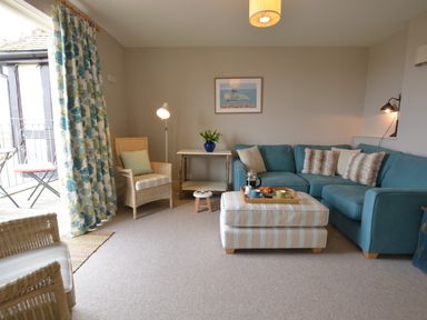 A living room with a blue sectional sofa and striped ottoman with a tray on top at Tamarisk Aldeburgh in Aldeburgh