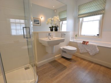 A bathroom with a shower cubicle, a wall-mounted sink, a toilet, and a bathtub with a towel and a book at Tamarisk, Aldeburgh in Aldeburgh