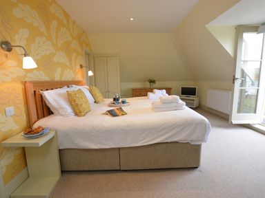 A bedroom with a double bed with white bedding and yellow pillows near a yellow patterned wall at Tamarisk Aldeburgh in Aldeburgh