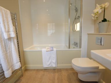A bathroom with a bathtub shower combination white towels on a radiator and a potted plant at Tamarisk Aldeburgh in Aldeburgh