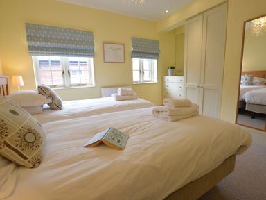 A bedroom with two single beds folded towels on the beds a book a chest of drawers a large mirror and two windows with patterned blinds at Tamarisk Aldeburgh in Aldeburgh