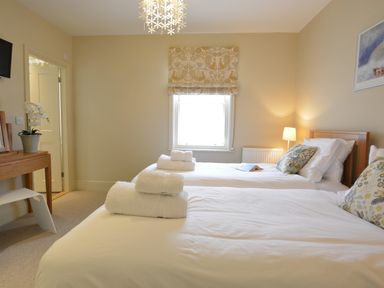 A bedroom with two single beds white linens and towels on each bed a window lamp a small desk with a plant and a stool at Tamarisk Aldeburgh in Aldeburgh