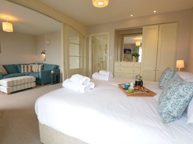 A bedroom with a bed and tray of breakfast with towels folded on the bed and a sitting area with sofa and ottoman at Tamarisk Aldeburgh in Aldeburgh