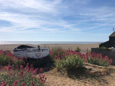 A small boat named Jill Anne Ipswich on a beach surrounded by pink flowers and a clear blue sky at Tamarisk Aldeburgh in Aldeburgh