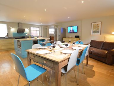 A kitchen dining area with a wooden table set with plates and wine glasses blue and white chairs and a brown sofa at Tamarisk Aldeburgh in Aldeburgh