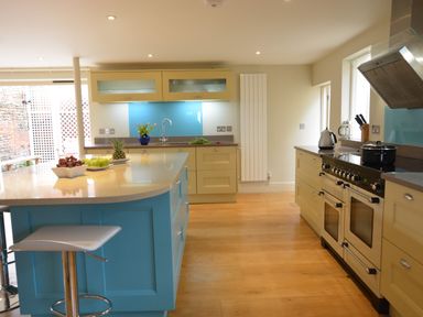 A kitchen with a blue island counter stools and cream cabinets at Tamarisk Aldeburgh in Aldeburgh
