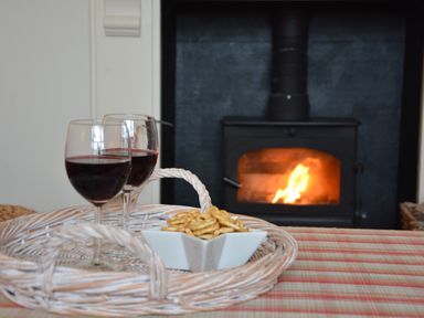 Two glasses of red wine and a bowl of snacks on a wicker tray in front of a fireplace at Tamarisk Aldeburgh