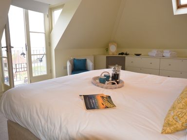 A bedroom with a bed a blue chair a dresser with towels and a balcony at Tamarisk Aldeburgh