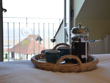 A tray with a coffee press and two cups on a bed near a balcony with a view of rooftops and the sea at Tamarisk Aldeburgh in Aldeburgh
