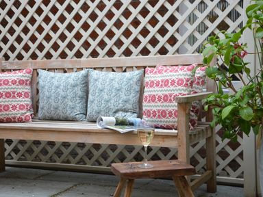 A wooden bench with patterned cushions a magazine and a glass of white wine on a wooden stool beside a plant at Tamarisk Aldeburgh in Aldeburgh