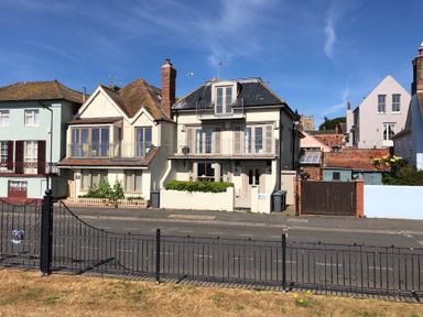 A row of houses with balconies and chimneys facing a street with a black metal fence at Tamarisk Aldeburgh in Aldeburgh