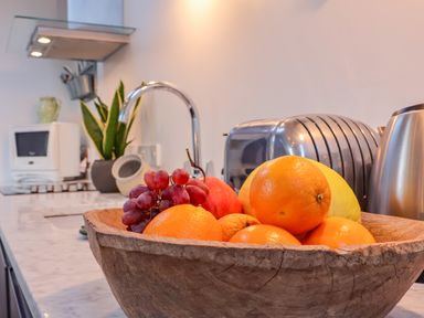 A kitchen countertop with a wooden bowl of fruit including oranges grapes and an apple at The Bothy at Snape Hall in Snape Suffolk