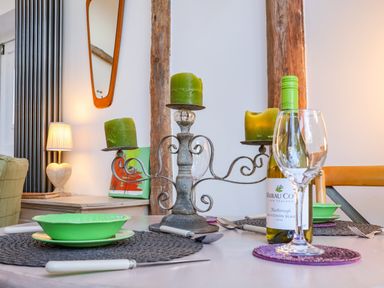 A dining table set with green bowls, wine bottle, wine glass, green candles on candelabra, and utensils at The Bothy at Snape Hall in Snape Suffolk