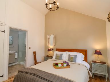 A bedroom with a double bed bedside tables and lamps and an open door to a bathroom at The Bothy at Snape Hall in Snape Suffolk
