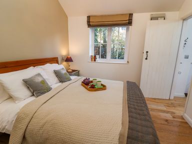 A bedroom with a bed bedside table lamp window and wooden floor at The Bothy at Snape Hall in Snape Suffolk