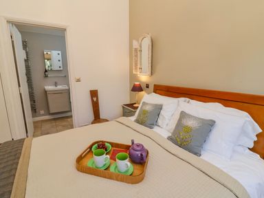 A bedroom with a bed with pillows and a tray with cups and a teapot and an open door to a bathroom at The Bothy at Snape Hall in Snape Suffolk