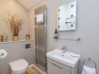 A bathroom with a toilet, a sink with a mirror above, a towel rail, and decorative jars with branches on a shelf at The Bothy at Snape Hall in Snape Suffolk
