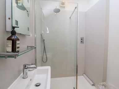 A bathroom with a sink a mirror a glass shower enclosure and a showerhead at The Bothy at Snape Hall in Snape Suffolk