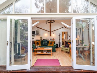 A living room with an open glass door showing a green sofa with yellow pillows a wooden coffee table and an armchair at The Bothy at Snape Hall in Snape Suffolk