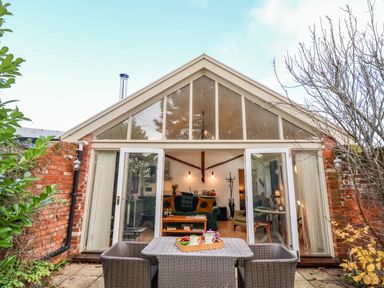 A patio area with a table and chairs outside glass doors leading to a living room at The Bothy at Snape Hall in Snape Suffolk