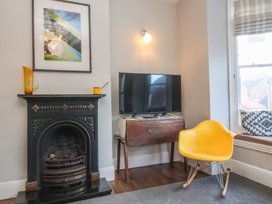A yellow chair next to a window and a television on a wooden table beside a black fireplace at Osprey in Southwold