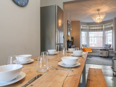 A dining table set with white bowls and glasses in a room with a window seat and an orange chair at Osprey in Southwold