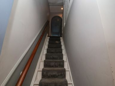 A staircase with dark carpet and wooden handrail between plain walls at Osprey in Southwold