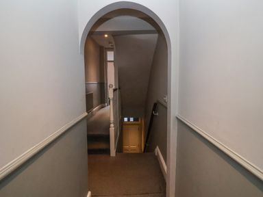 A hallway with an arched doorway leading to a staircase with a handrail and a door at the bottom at Osprey in Southwold
