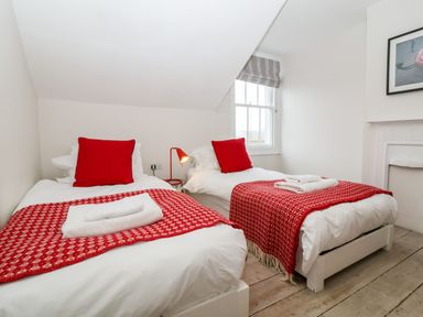 A bedroom with two single beds red blankets and pillows a bedside table and a window at Osprey in Southwold