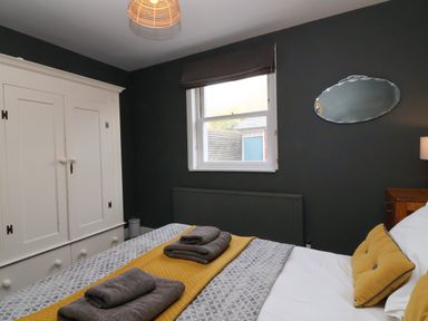 A bedroom with a bed having gray and yellow bedding a white wardrobe and a window at Kestrel in Southwold