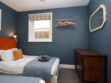 A bedroom with two single beds a wooden dresser a window with a blind and wall-mounted hangers at Kestrel in Southwold