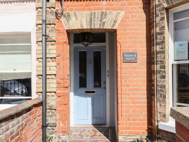 A blue front door numbered 3 with a tiled entrance and a sign reading Osprey and Kestrel at a brick building in Southwold