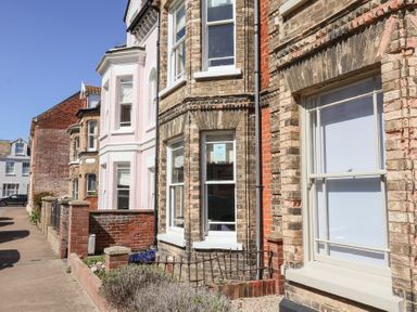 A row of brick and painted houses with bay windows and small front gardens on a residential street