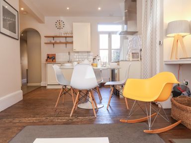 A kitchen and dining area with white chairs around a table and a yellow rocking chair at Kestrel in Southwold