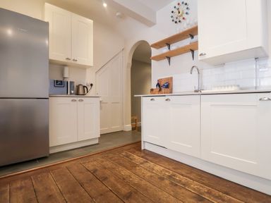 A kitchen with white cabinets a stainless steel refrigerator wooden floor and an arched doorway at Kestrel in Southwold