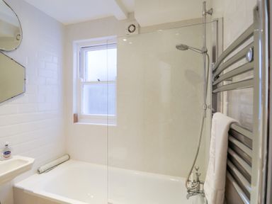 A bathroom with a bathtub and shower fixture a window and a towel on a heated towel rail at Kestrel in Southwold